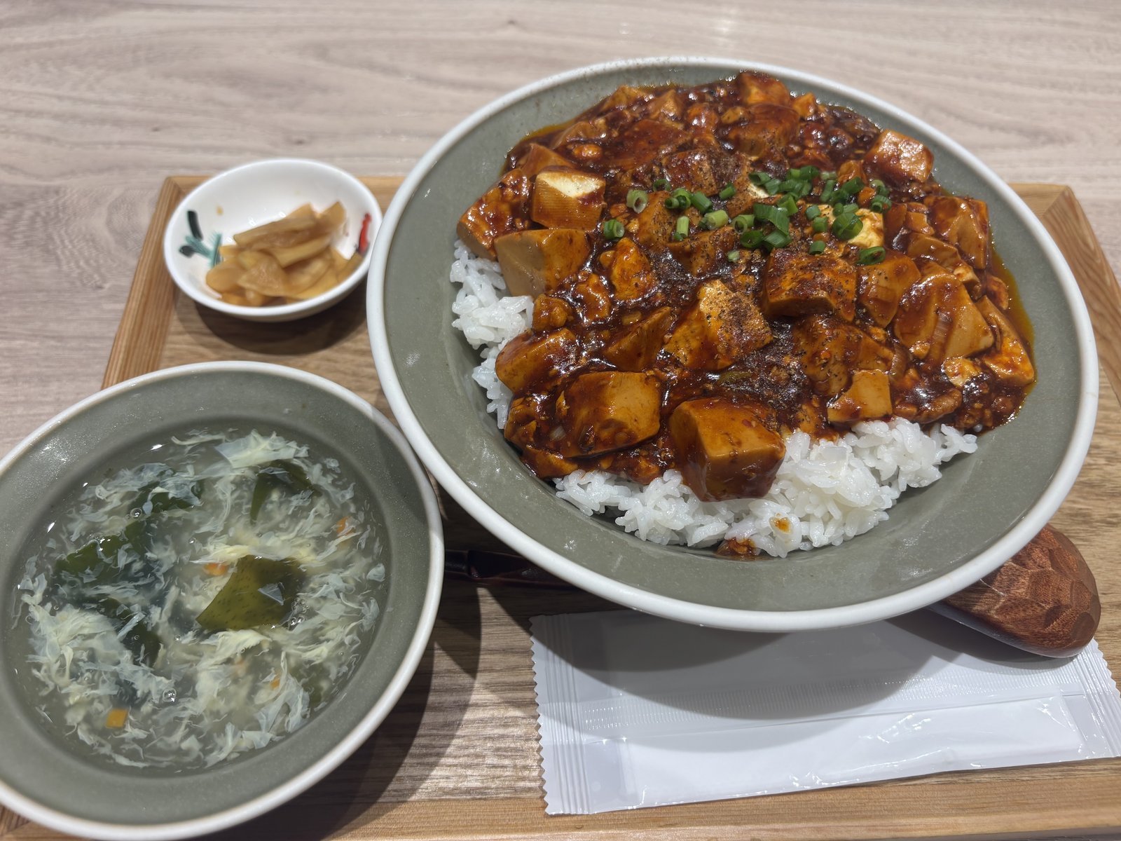 麻婆豆腐丼、卵スープ、小鉢の漬物がトレーに並ぶ