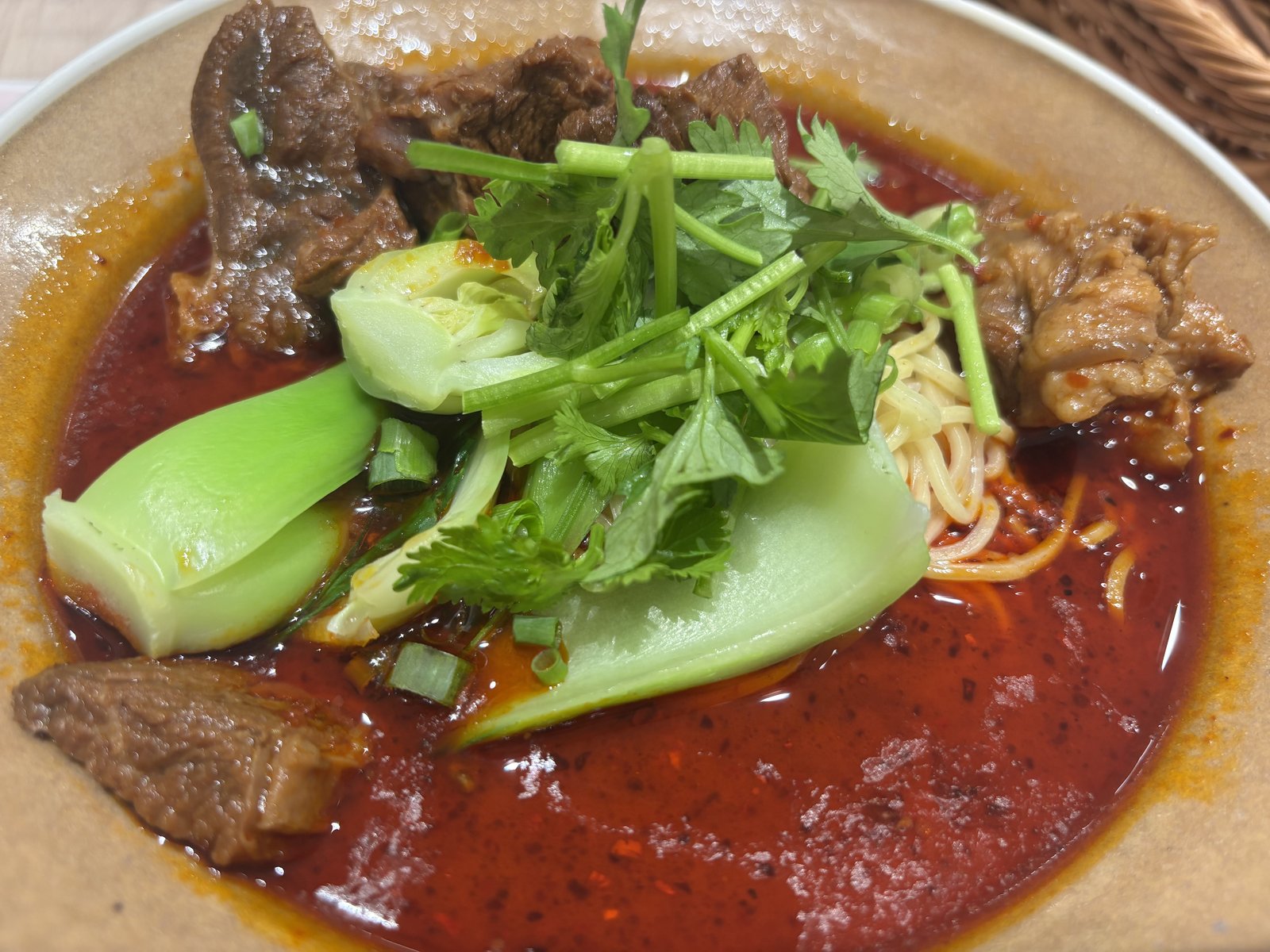 麻辣牛肉麺。牛肉、パクチー、青菜、麺が赤いスープに入っている